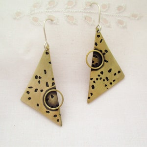 May include: A pair of gold triangle earrings with a textured surface and a circular cutout. The earrings have a silver hook closure.