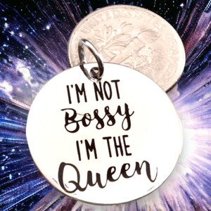 May include: A silver charm with the text "I'm not bossy I'm the Queen" in black lettering.