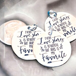 May include: Three round silver tags with a black inscription that reads "Every love story is beautiful but ours is my favorite".