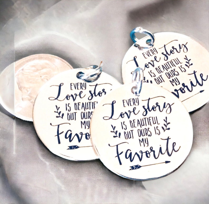 May include: Three round silver tags with a black inscription that reads "Every love story is beautiful but ours is my favorite".