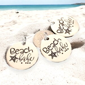 Puede incluir: Tres dijes redondos plateados con el texto "Beach babe" y un peque&ntilde;o dise&ntilde;o de estrella de mar.