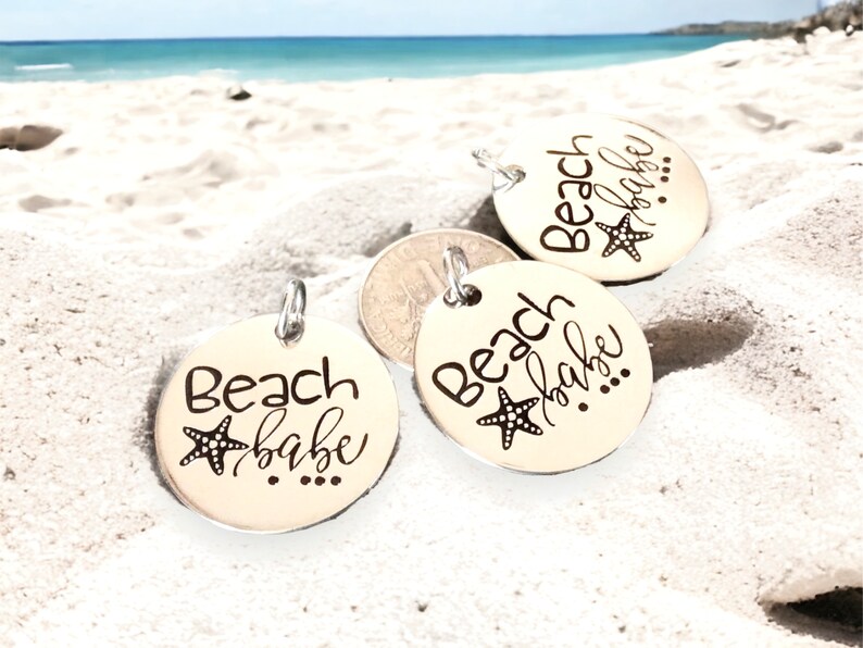 Puede incluir: Tres dijes redondos plateados con el texto "Beach babe" y un peque&ntilde;o dise&ntilde;o de estrella de mar.