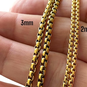 May include: Two gold chains, one 3mm and one 2mm in width, are shown side-by-side on a person's hand.