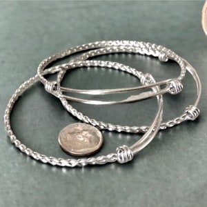 May include: Three silver bangle bracelets with a twisted rope design. The bracelets have small, round knots at the ends.
