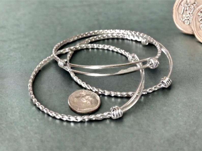 May include: Three silver bangle bracelets with a twisted rope design. The bracelets have small, round knots at the ends.