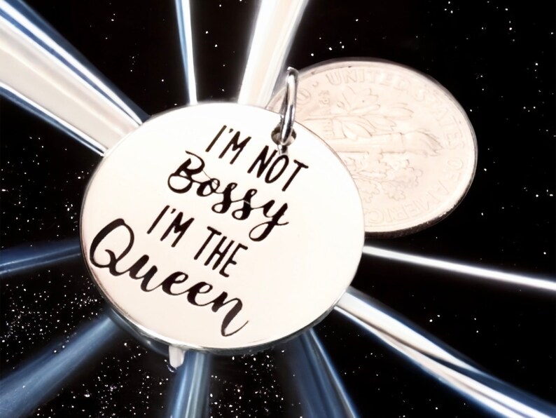 May include: Silver charm with the text "I'm not bossy I'm the Queen" in black lettering.