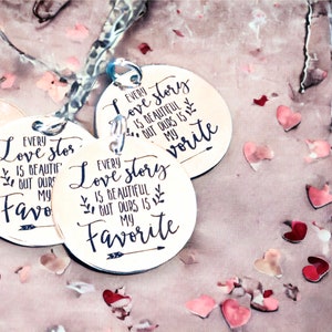 May include: Three round wooden signs with the text "Every love story is beautiful but ours is my favorite" on each sign. The signs are on a pink surface with pink and red confetti hearts.