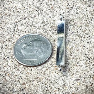 May include: Silver metal bar with rounded ends and two small loops. The bar is about the size of a US dime.