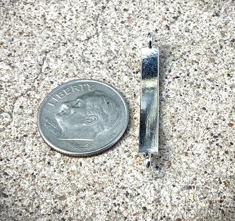 May include: Silver metal bar with rounded ends and two small loops. The bar is about the size of a US dime.
