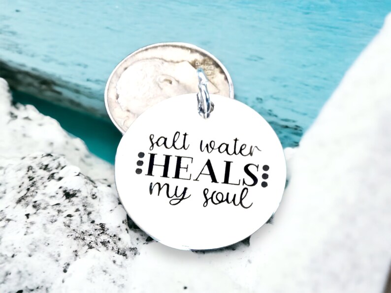 May include: A silver charm with the text "salt water ::HEALS:: my soul" on a white background.