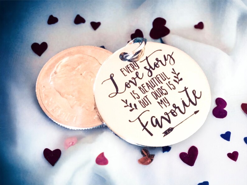 May include: A round silver charm with the text "Every love story is beautiful but ours is my favorite" engraved on it. The charm is surrounded by small red and blue hearts.