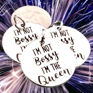 May include: Three silver round charms with the text "I'm not bossy I'm the queen" on them.