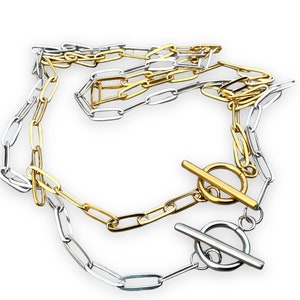 May include: A two-tone necklace with a silver and gold chain link design. The necklace features a toggle clasp in both silver and gold. The jewelry is displayed on a white background.