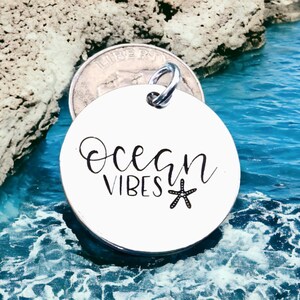 May include: A white round metal charm with the text "Ocean Vibes" and a black starfish design.