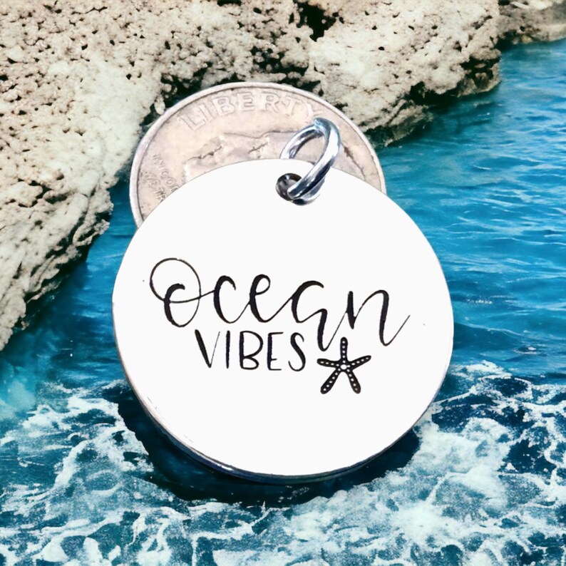 May include: A white round metal charm with the text "Ocean Vibes" and a black starfish design.