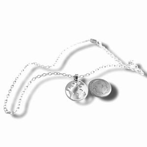 May include: A silver-colored necklace featuring a pendant in the shape of a globe. The pendant is round with cut-out continents. A U.S. dime is next to the pendant for size comparison. The necklace chain is also silver.