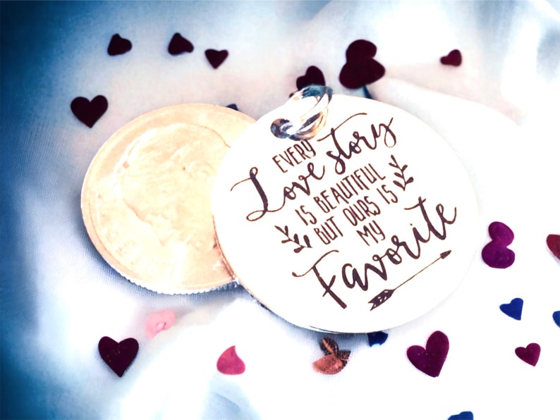 May include: A white wooden round ornament with a brown inscription that reads "Every love story is beautiful but ours is my favorite". The ornament is surrounded by small hearts of various colors.
