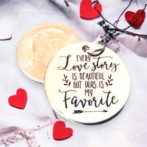 May include: A gold-colored round keychain with the text "Every love story is beautiful but ours is my favorite" engraved on it. The keychain has a small arrow design below the text.
