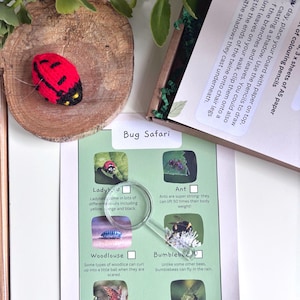A flat lay arrangement showing a bug safari scavenger hunt with a magnifying glass. The scene is decorated with green leaves and a wooden disc arranged on a white background and a knitted ladybird.