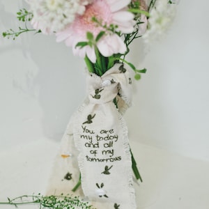 以下が含まれることがあります： ピンクと白の花束で、クリーム色のリボンで結ばれています。リボンには小さな緑色の鳥のイラストと、「You are my today and all of my tomorrows」という刺繍が施されています。