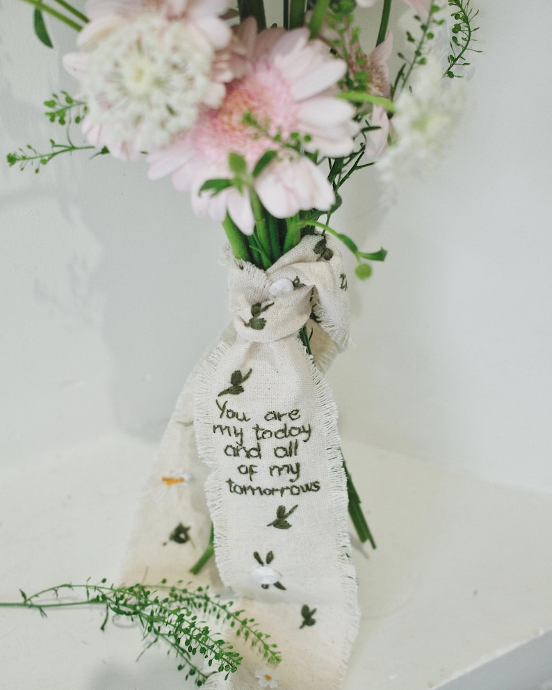 以下が含まれることがあります： ピンクと白の花束で、クリーム色のリボンで結ばれています。リボンには小さな緑色の鳥のイラストと、「You are my today and all of my tomorrows」という刺繍が施されています。