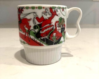 May include: White ceramic Christmas mug featuring Santa Claus in his sleigh with reindeer, gifts, and decorative green and red accents. The mug has a unique handle design and a ribbed base, perfect for holiday beverages.