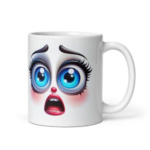 May include: White ceramic mug featuring a cartoon face printed on it. The face has large blue eyes, red lips, and a surprised expression.