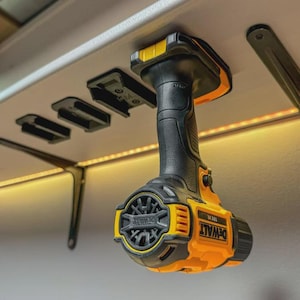 May include: A black and yellow DeWalt 18V cordless drill suspended from a ceiling-mounted holder. The drill is black with yellow detailing and the DeWalt logo. The holder is black and attached to a white surface.