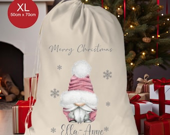 May include: A cream-coloured drawstring gift sack featuring a printed illustration of a gnome wearing a pink hat and white beard, surrounded by snowflakes. The text reads Merry Christmas and Ella-Anne. The sack measures 50cm x 70cm in size.