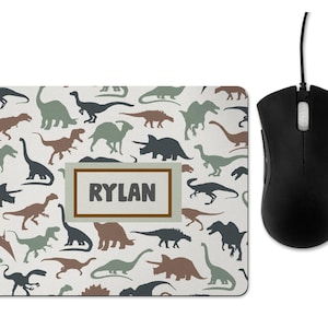 May include: A white mouse mat with a pattern of brown, green and black dinosaur silhouettes. The text "RYLAN" is printed in a brown rectangle in the centre of the mouse mat.