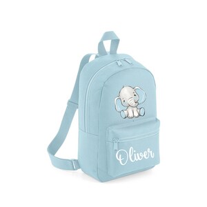 May include: A pale blue backpack with a cartoon elephant design. The bag has a front zipped pocket and adjustable straps. The name "Oliver" is printed in white script on the front. This backpack is suitable for young children.