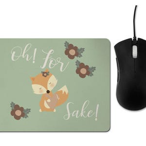 May include: A green mouse mat with a cute fox illustration and the text "Oh! for Sake!" in white. The fox is holding a heart and has a flower on its head. There are brown flowers with green leaves on the mouse mat.