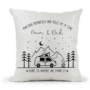May include: White cushion with black text that reads "Making memories one mile at a time Mum & Dad" and a black illustration of a camper van, mountains, trees, and a campfire. The text at the bottom reads "Home is where we park it."