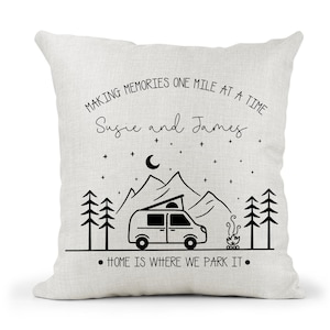 May include: A white throw pillow with black text that reads "Making memories one mile at a time Susie and James. Home is where we park it."  The pillow features a black and white illustration of a camper van, mountains, trees, and a campfire.