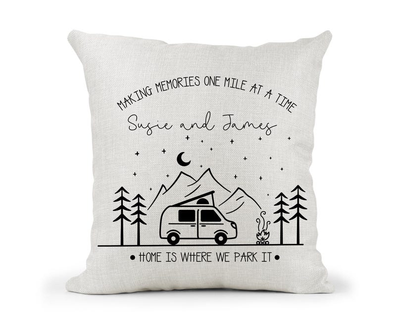May include: A white throw pillow with black text that reads "Making memories one mile at a time Susie and James. Home is where we park it."  The pillow features a black and white illustration of a camper van, mountains, trees, and a campfire.