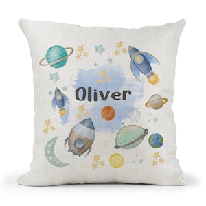 May include: A white pillow with a space theme design. It features rockets, planets, stars, and the name "Oliver".