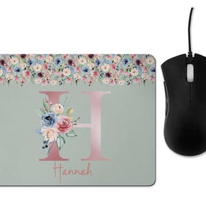 May include: A light green mouse mat with a floral border and a pink letter H with a floral design. The name Hannah is written below the letter.