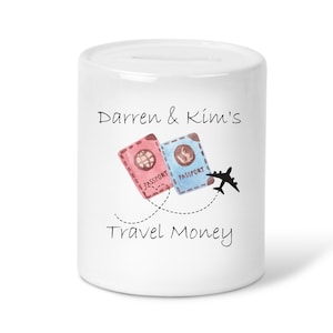 May include: White ceramic money box with a travel theme. It has a slot on the top for coins and says "Darren & Kim's Travel Money" on the front. There are two passports and a plane on the front.