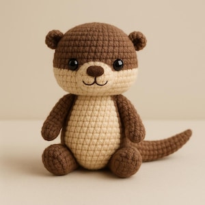 Op de afbeelding: Een handgemaakte gehaakte otter in bruin- en beigetinten. De otter heeft een gedetailleerd, getextureerd uiterlijk met een ronde kop, kleine oren en een lachend gezicht. De knuffel zit rechtop met zijn staart uitgestrekt.