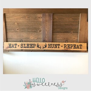 May include: Wooden sign with the text "Eat. Sleep. Hunt. Repeat" with a pair of antlers between the words "Sleep" and "Hunt".