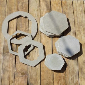Könnte beinhalten: Eine Sammlung grauer, geometrischer Untersetzer und Untersetzer. Das Set enthält sechseckige und einzigartig geformte Teile, die auf einer verwitterten Holzoberfläche angeordnet sind. Die neutrale Farbpalette und das natürliche Material deuten auf eine rustikale oder minimalistische Ästhetik hin.