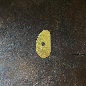 Peut inclure: Petit objet jaune en forme de goutte d'eau avec un trou près du sommet. L'objet a une surface texturée et se détache sur un fond sombre et moucheté.