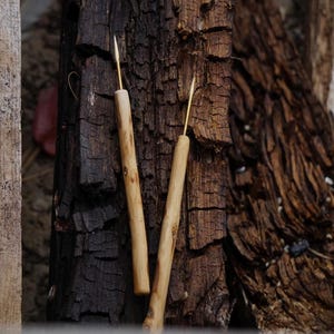 Puede incluir: Dos leznas de madera hechas a mano con puntas de latón, sobre un fondo de corteza de árbol texturizada. Las leznas tienen mangos de madera de color claro y están diseñadas para la artesanía o el trabajo en cuero.
