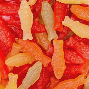 Könnte beinhalten: Nahaufnahme eines Haufens von Gummibonbons in Fischform. Die Süßigkeiten sind in Rot-, Orange- und Gelbtönen gehalten. Einige tragen den Aufdruck "Mala".