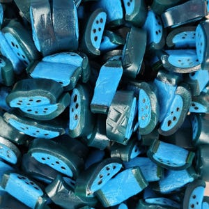 May include: A collection of small, blue, semi-circular candy pieces featuring a dark blue rind and a lighter blue interior with small black dots representing seeds. The candies are densely packed together, showing various cross-sections and shapes.