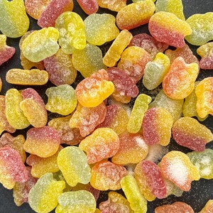 May include: A variety of colorful, chewy candies in various shapes, including hearts, stars, and swirls. The candies are arranged in a random pattern on a dark surface.