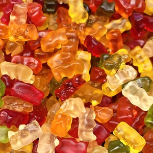 Può includere: Primo piano di un mucchio di caramelle gommose a forma di orsetto colorate. Gli orsetti sono in varie tonalità di rosso, arancione, giallo e verde. Le caramelle sono traslucide e hanno un aspetto lucido.