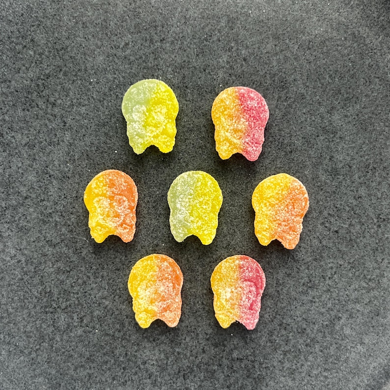 May include: Seven yellow, orange, and pink skull-shaped candies on a gray surface.