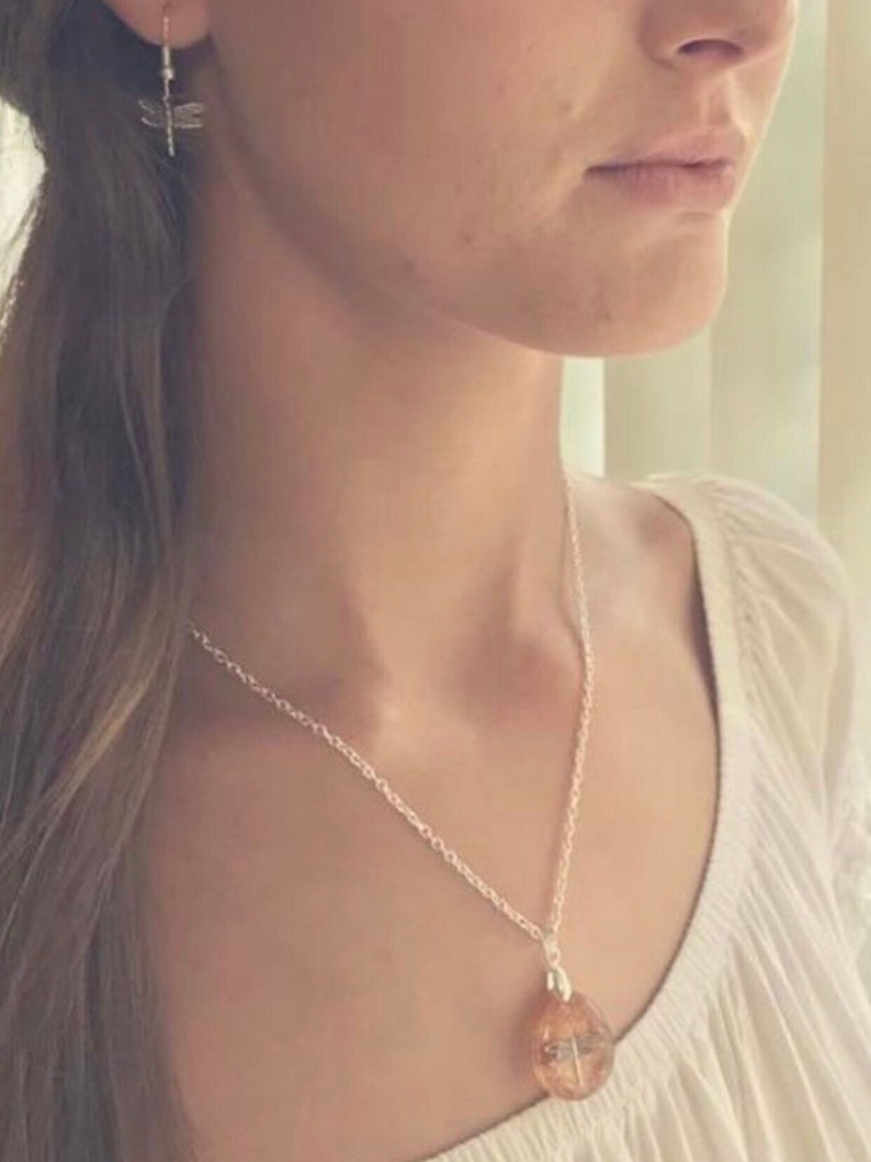 May include: A silver necklace with a clear pendant featuring a dragonfly design. The pendant is a round, flat shape with a silver chain.