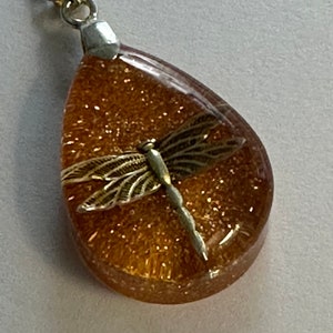 May include: A gold dragonfly pendant necklace with a teardrop-shaped resin charm filled with gold glitter.